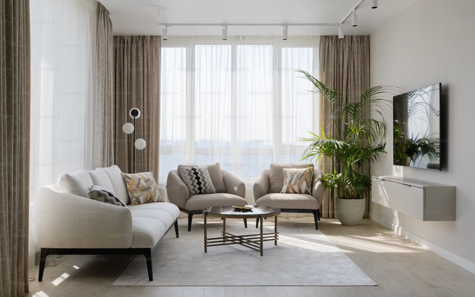 Living de una vivienda con cortinas claras, sillones beige y una planta, iluminado por luz natural